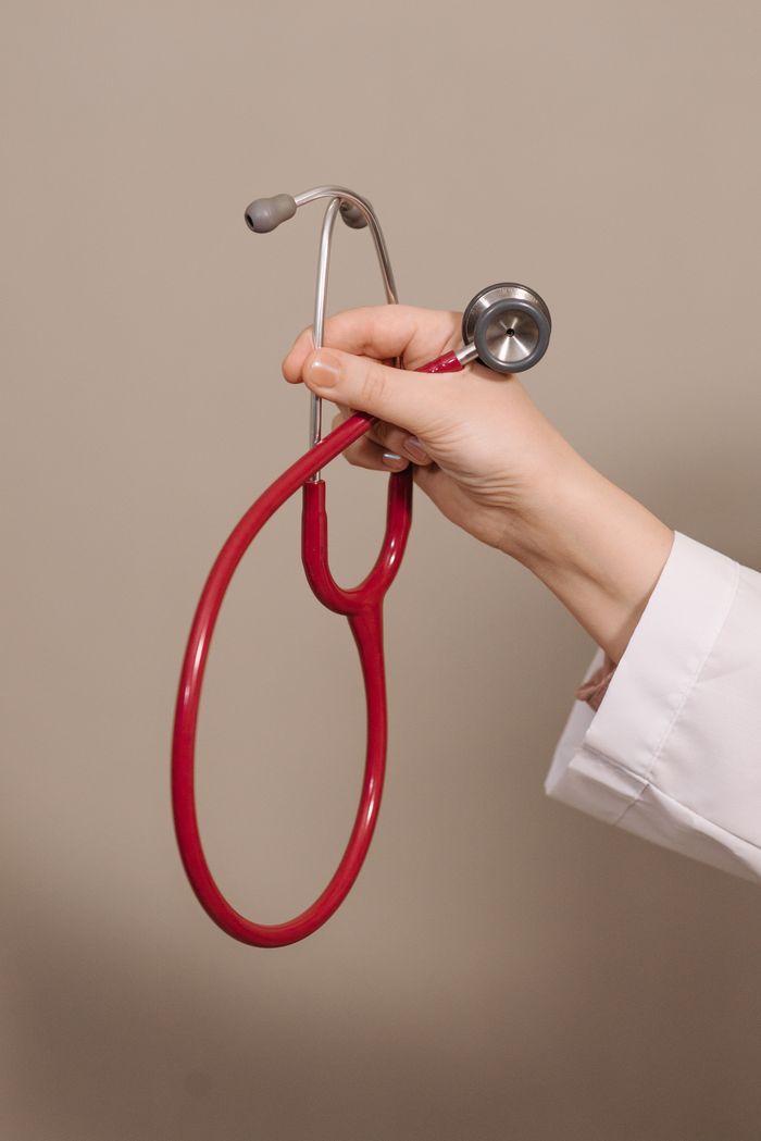 A close-up shot of a hand holding a red stethoscope against a plain background, emphasizing medical themes.